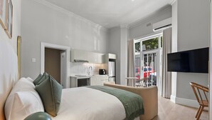 Habitación de hotel moderna con una cama grande, una kitchenette pequeña, un televisor de pantalla plana y un balcón con vistas.