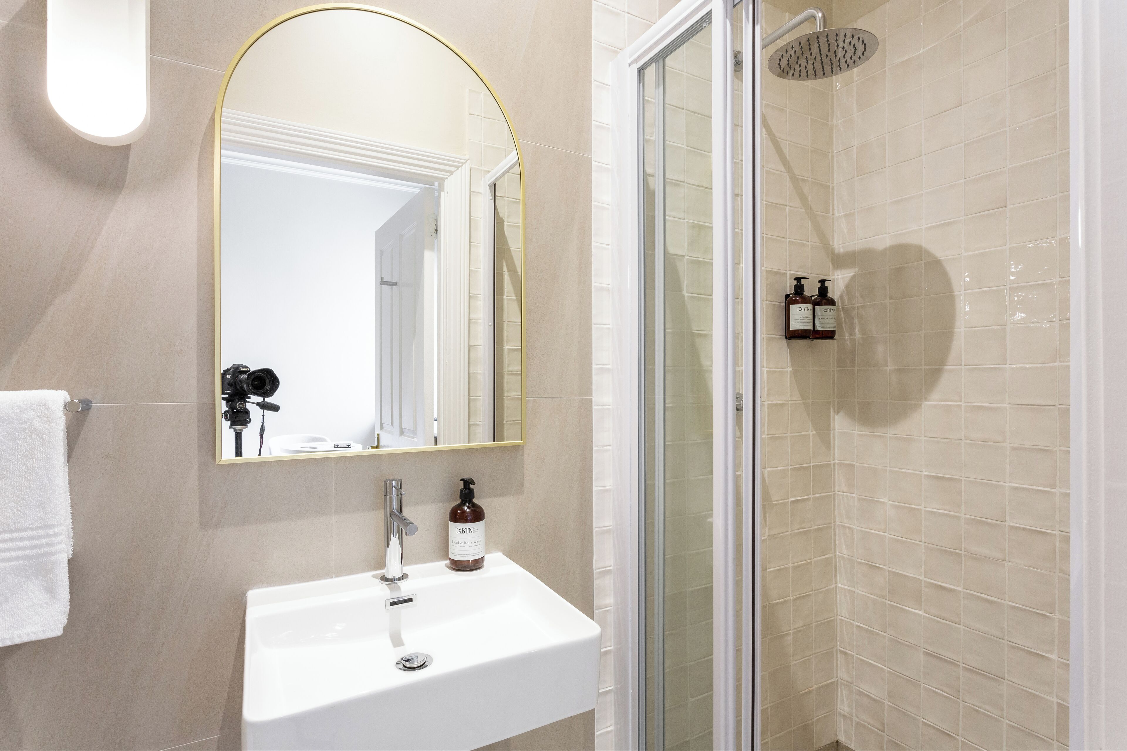 Ein Badezimmer mit einem weißen Waschbecken, einem Spiegel mit goldener Rahmung, einer Dusche mit Glastür und einem Handtuchhalter.