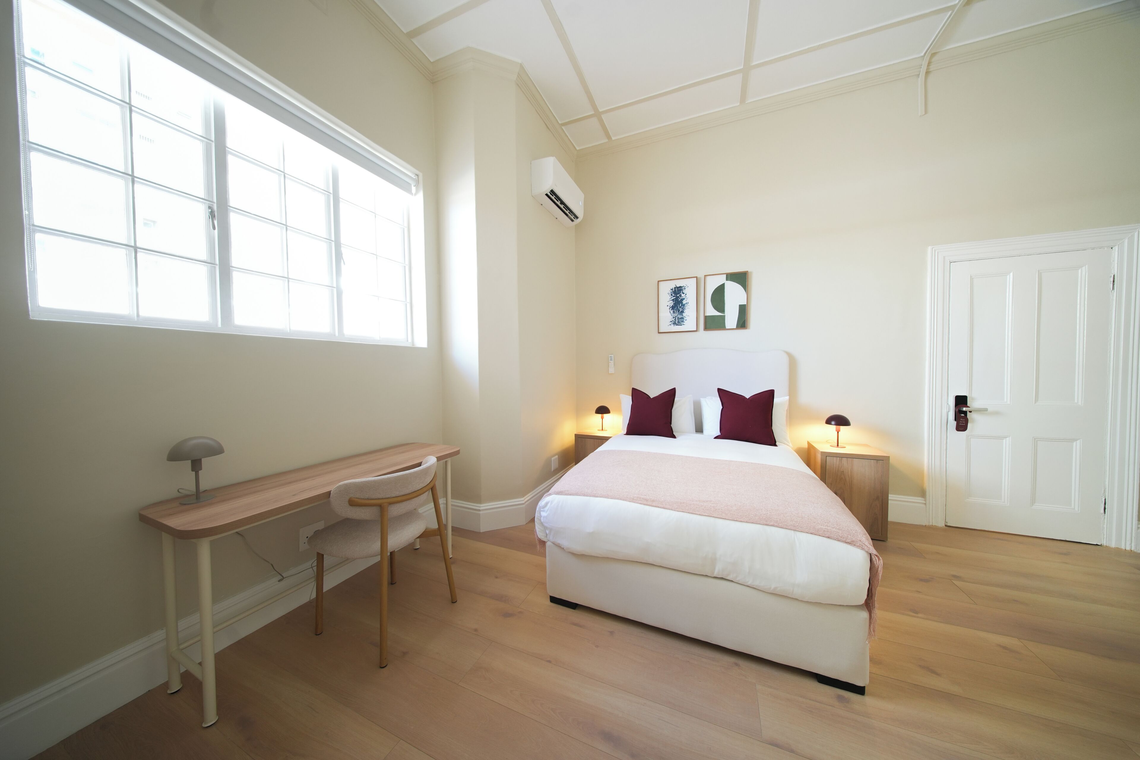 A bedroom with a bed, desk, chair, bedside lamps, and a window.