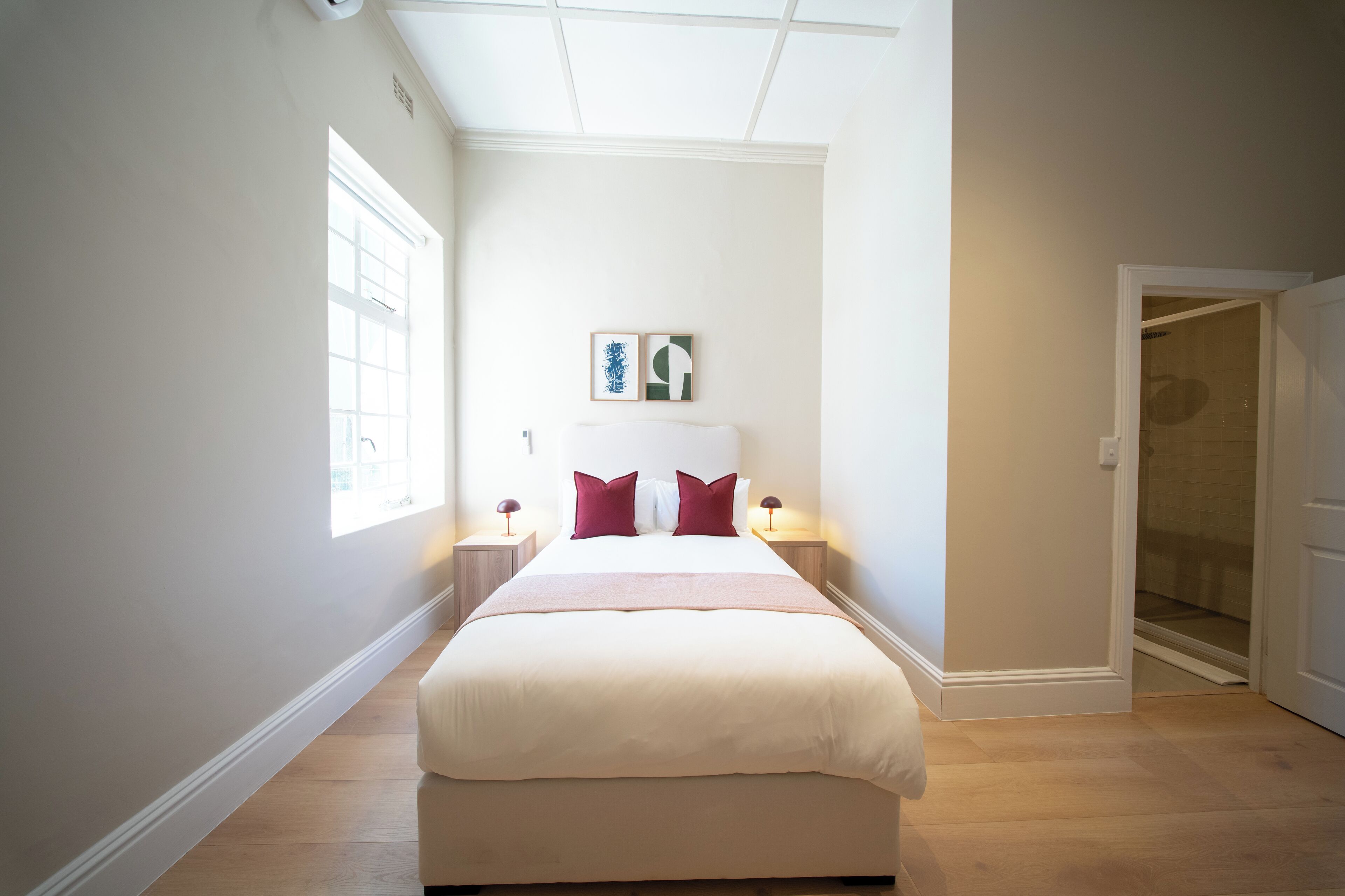Quarto com cama grande, abajures, janela e porta para o banheiro.