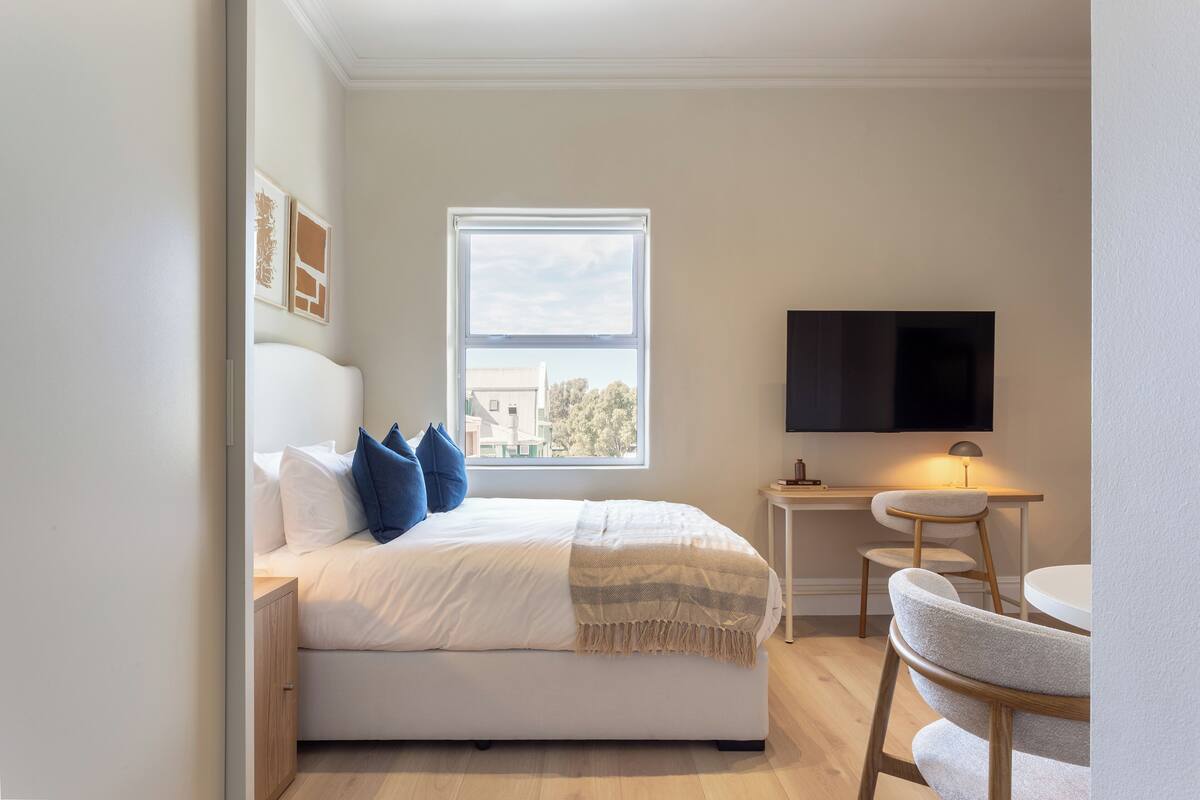 A bedroom with a bed, a TV, a desk, and a window.