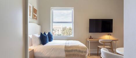 Un dormitorio con cama, televisión, escritorio y ventana.
