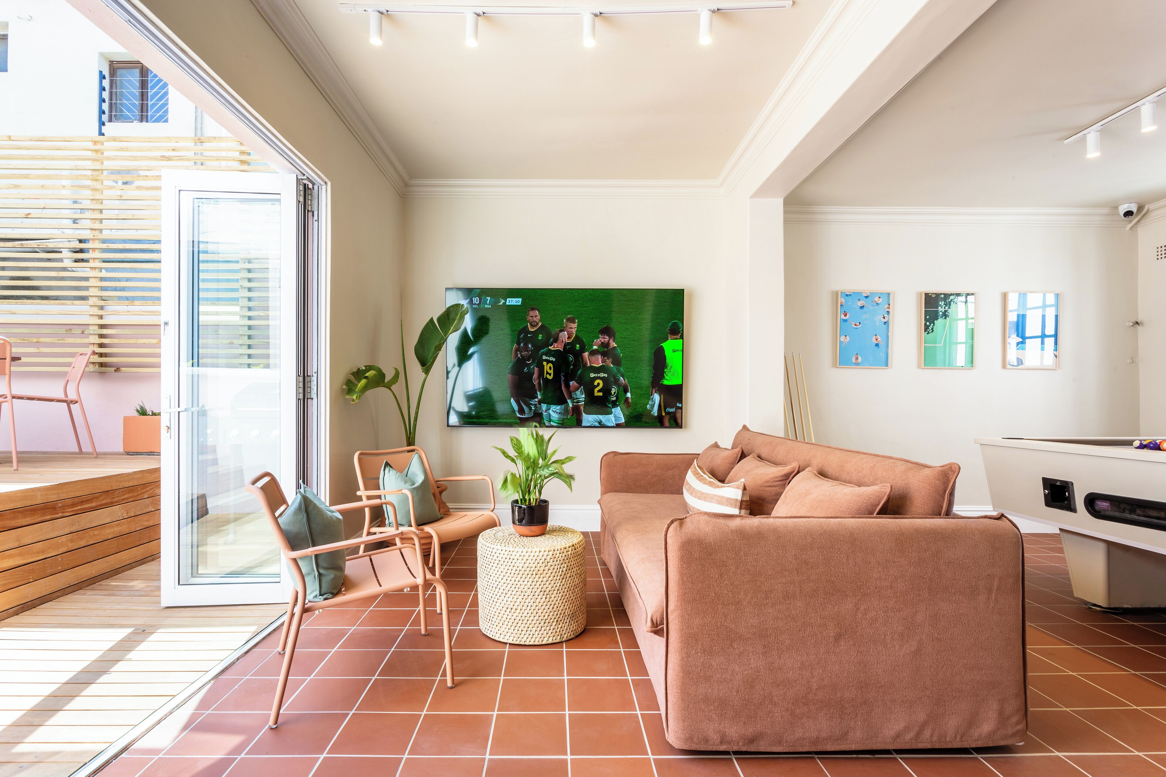A modern living room with a large flat-screen TV, a sofa, chairs, and a small side table.