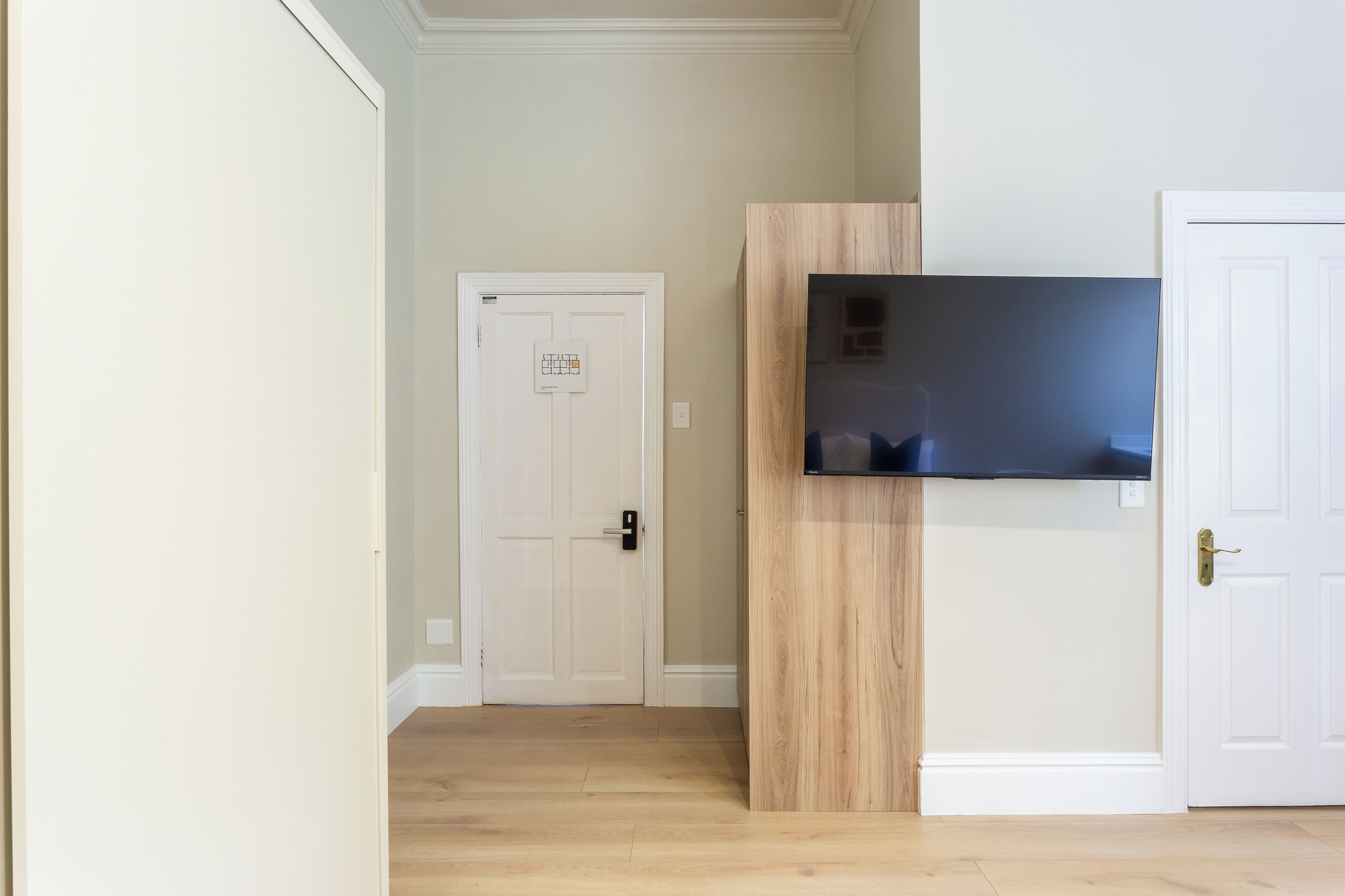 A hallway with a white door, a mounted flat-screen TV, and a wooden accent wall.