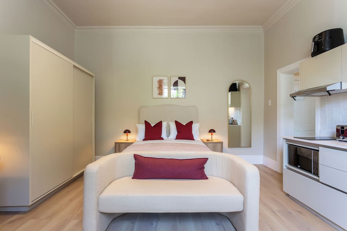 A modern bedroom with a large bed, bedside lamps, a built-in wardrobe, and a kitchenette.
