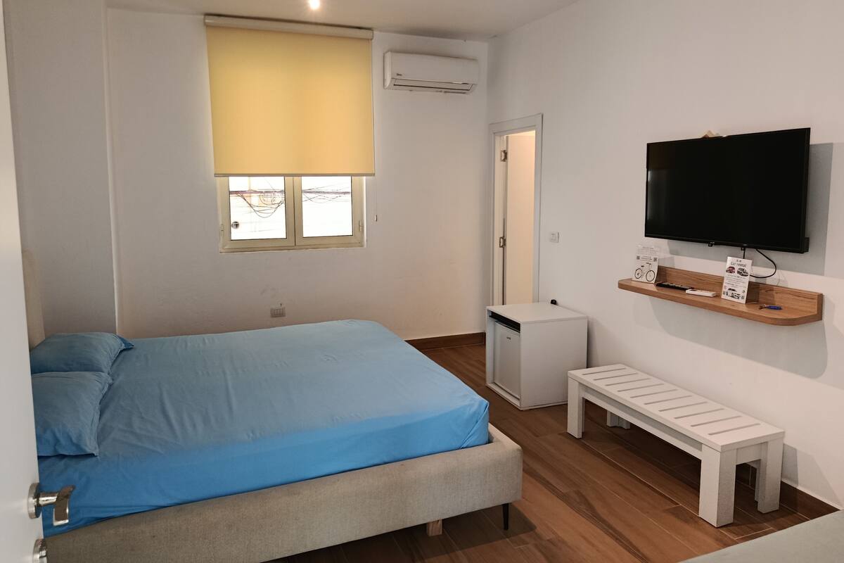 Une chambre à coucher avec un lit, un téléviseur fixé au mur, une petite table et un banc.