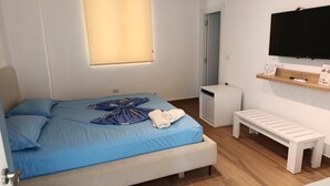 Una camera da letto con un letto, una panca, una televisione e un piccolo armadietto bianco.