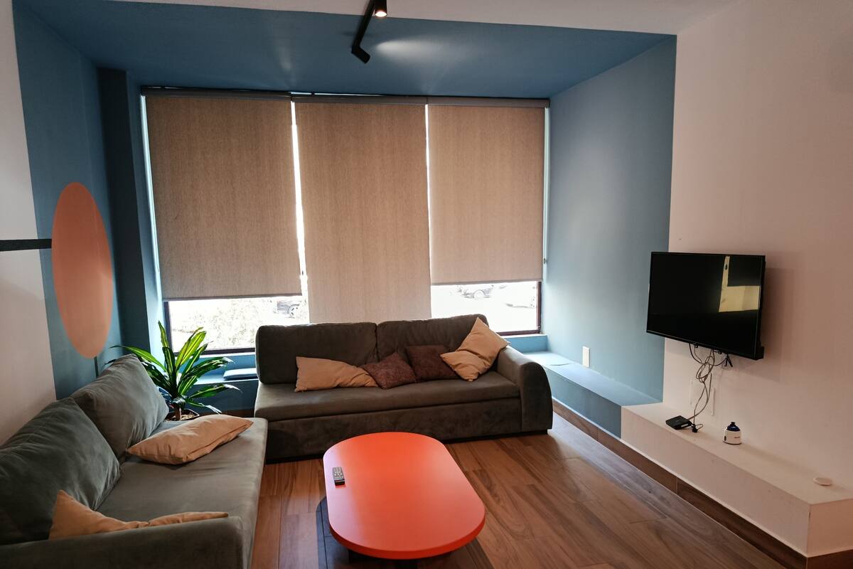 Un salon moderne avec un canapé, un pouf et un téléviseur fixé au mur.