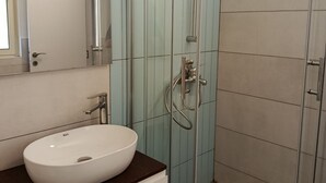 Un bagno moderno con un lavandino bianco, uno spazio doccia in vetro e pareti rivestite di piastrelle azzurrine.