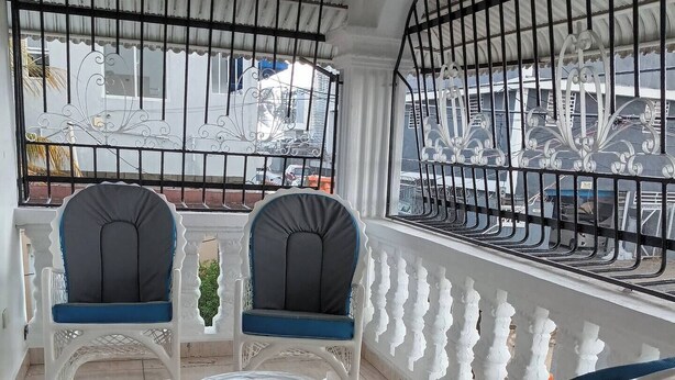 Un balcón con mobiliario de mimbre blanco, incluyendo dos sillas y una mesita.