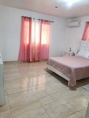Ein Schlafzimmer mit einem Bett, einem Nachttisch, einer Klimaanlage und einem Fenster mit rosa Vorhängen.