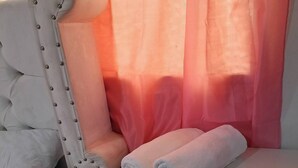Un dormitorio con una cama blanca, una silla blanca y una mesita de noche con cajones.