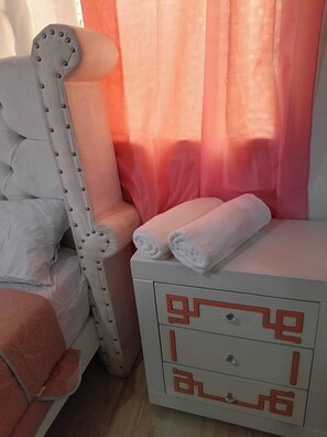 Ett sovrum med en vit säng, en vit stol och ett nattduksbord med lådor.