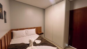 A bedroom with a wooden headboard, a bed with white linens, a brown knitted blanket, and a wooden nightstand. - Apto com 2 su tes a 100m do Japaratinga Resort (Japaratinga)