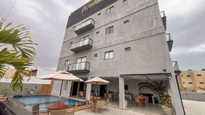 A modern building with a swimming pool, outdoor seating, and a balcony. - Apto com 2 su tes a 100m do Japaratinga Resort (Japaratinga)