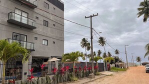 A modern building with balconies, a dirt road, and palm trees. - Apto com 2 su tes a 100m do Japaratinga Resort (Japaratinga)