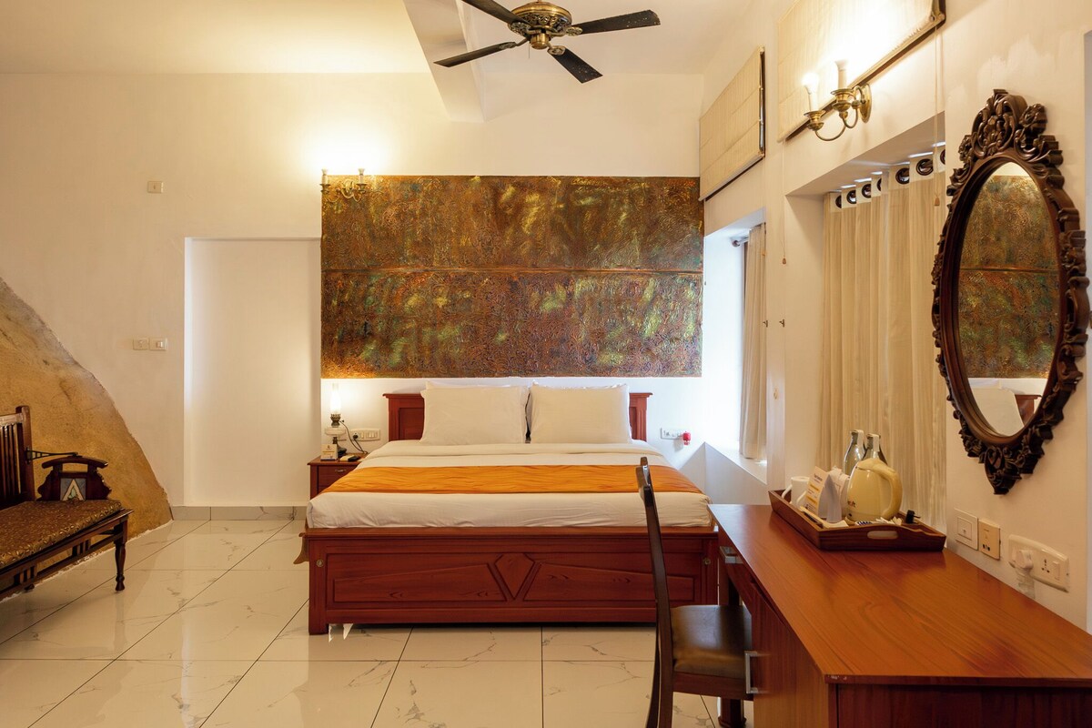 Ein Schlafzimmer mit Bett, Schreibtisch, Stuhl, Deckenventilator, einem großen Spiegel und einem Wandbild.