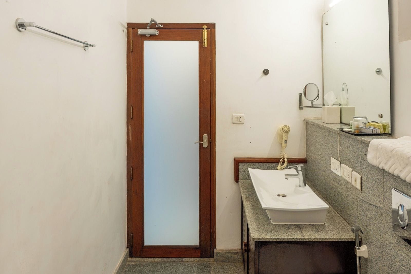 A bathroom with a wooden door, a towel rack, a sink with a mirror, and a hairdryer.