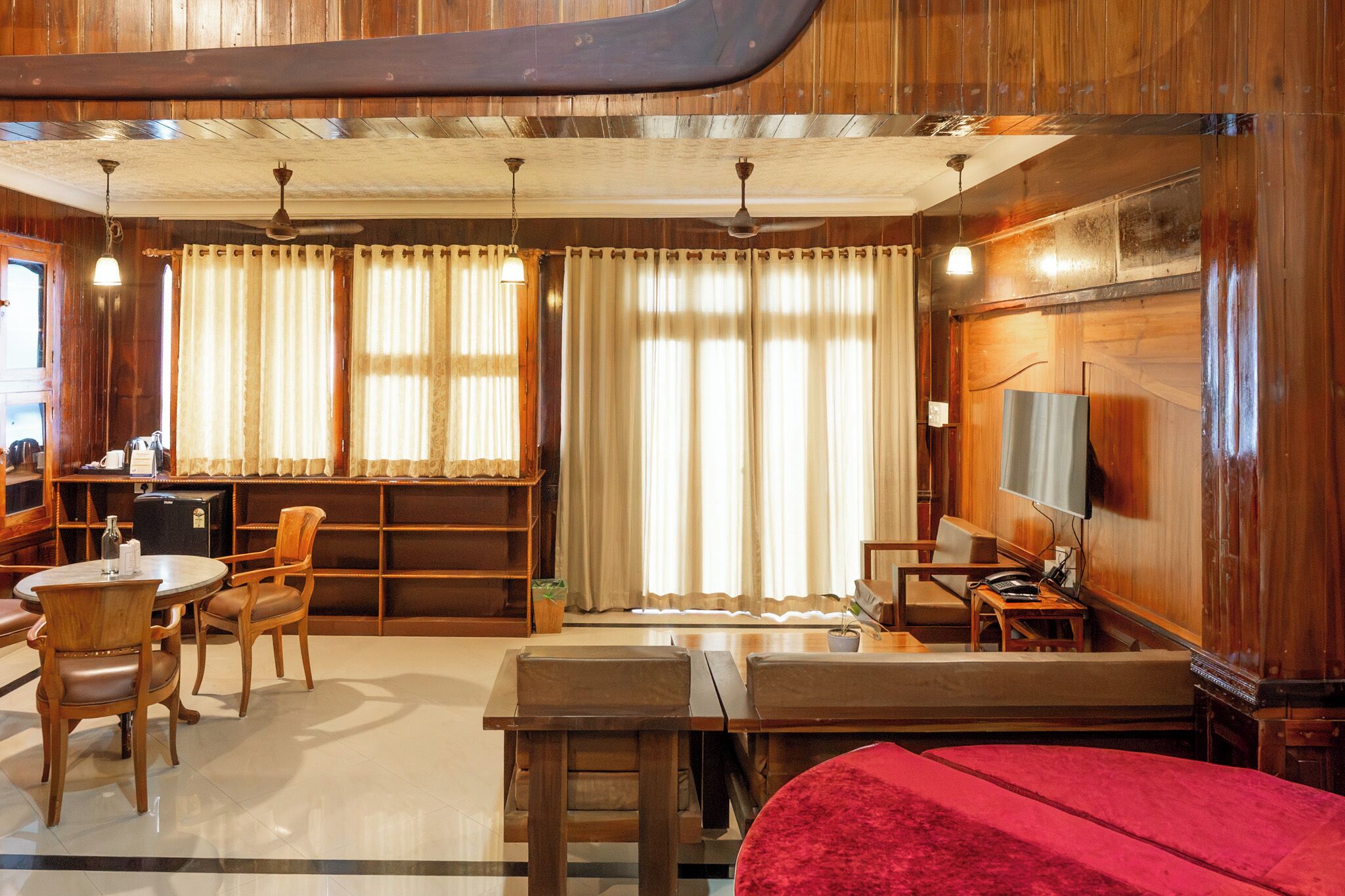 A wooden-furnished room with a sofa, chairs, a small table, a TV, and a bookshelf.