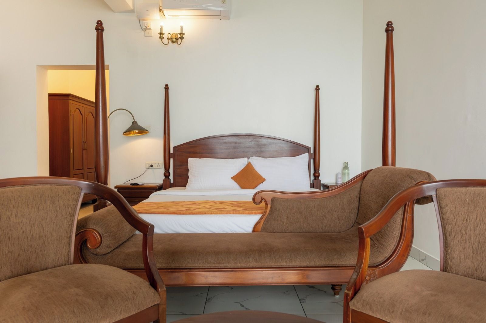 A four-poster bed with a wooden headboard, two nightstands, a lamp, and two upholstered chairs.