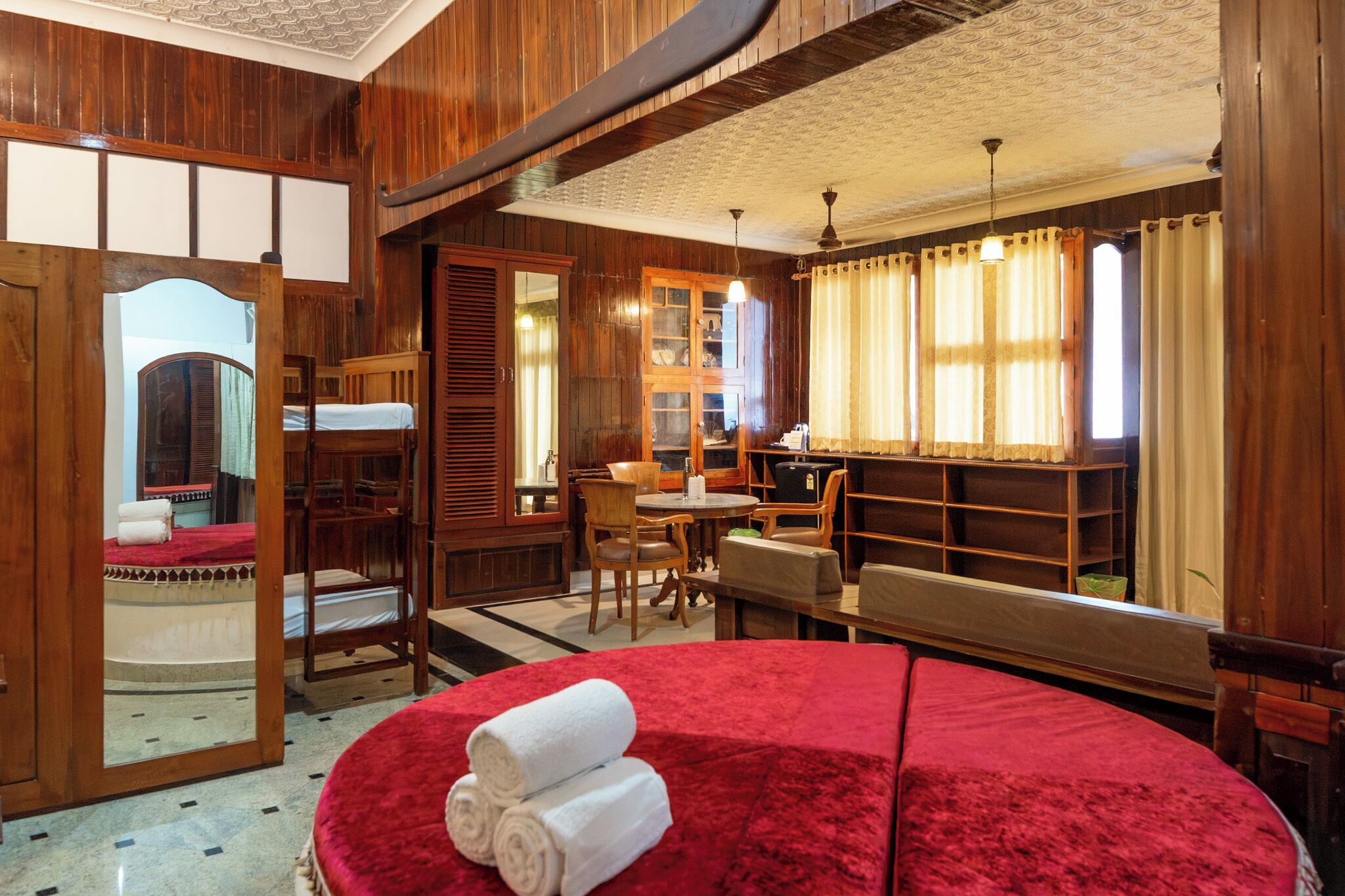 A room with a red carpet, wooden furniture, a bed with a red headboard, a wooden wardrobe, and a mirror.