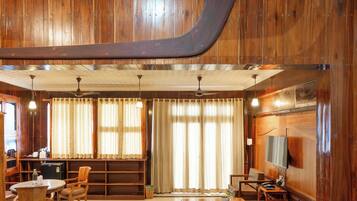Una habitación con paneles de madera, una viga de madera grande, un ventilador de techo, un televisor y una zona de estar con sillas y una mesa.