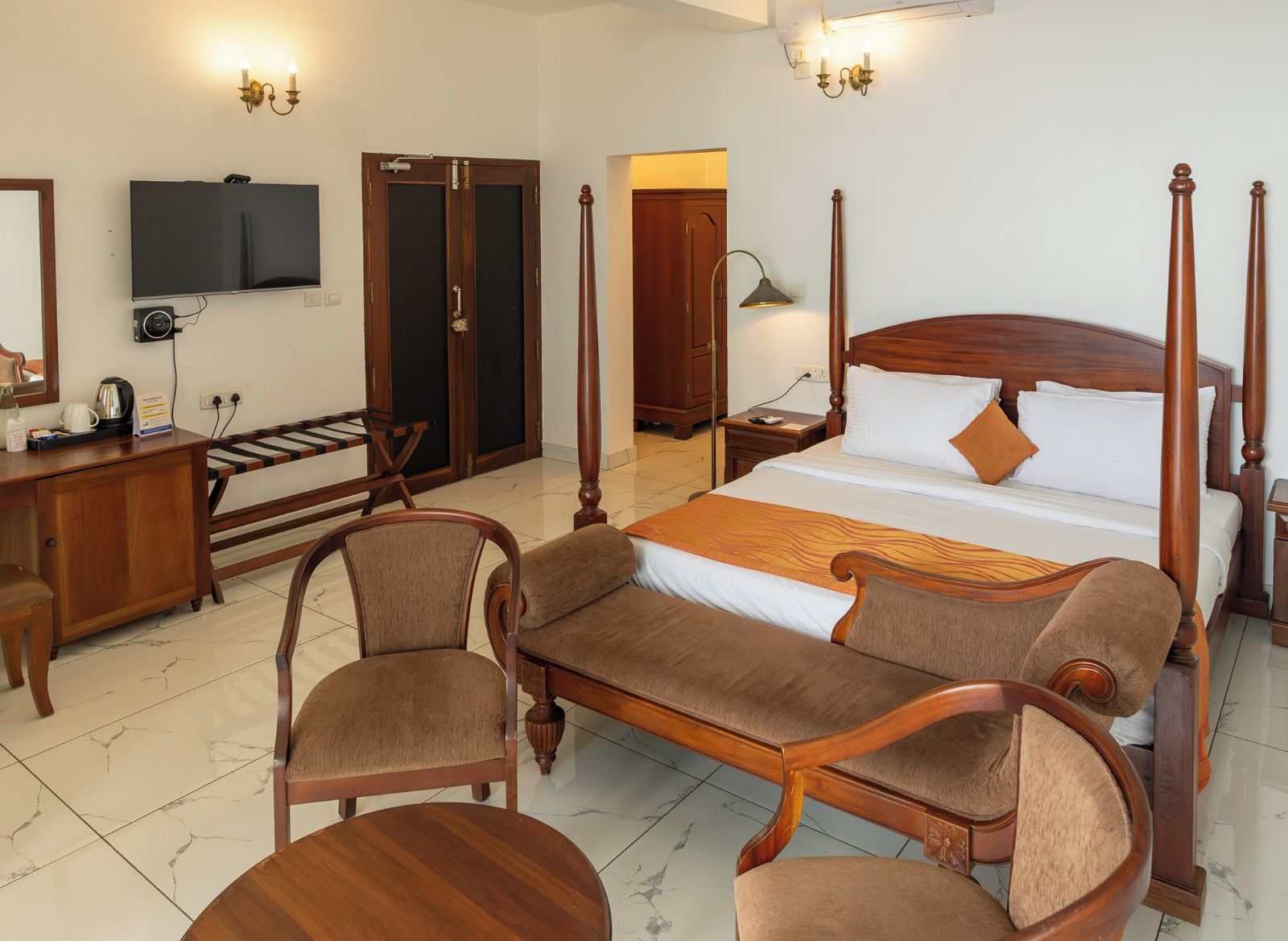 A hotel room with a four-poster bed, a desk with a chair, a television, and a wardrobe.