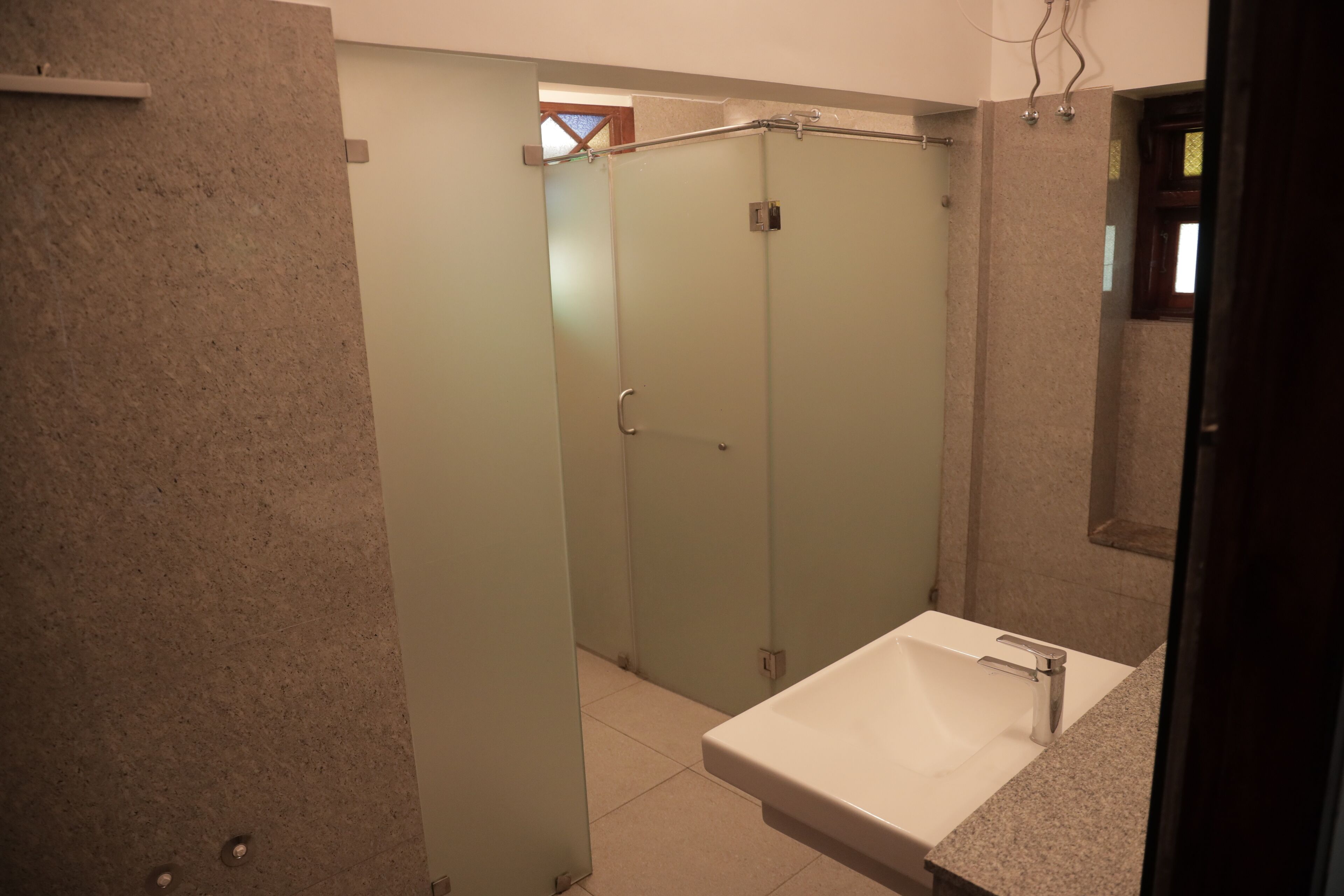 A bathroom with a white sink, frosted glass shower doors, and a tiled floor.