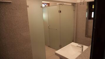 A bathroom with a white sink, frosted glass shower doors, and a tiled floor.