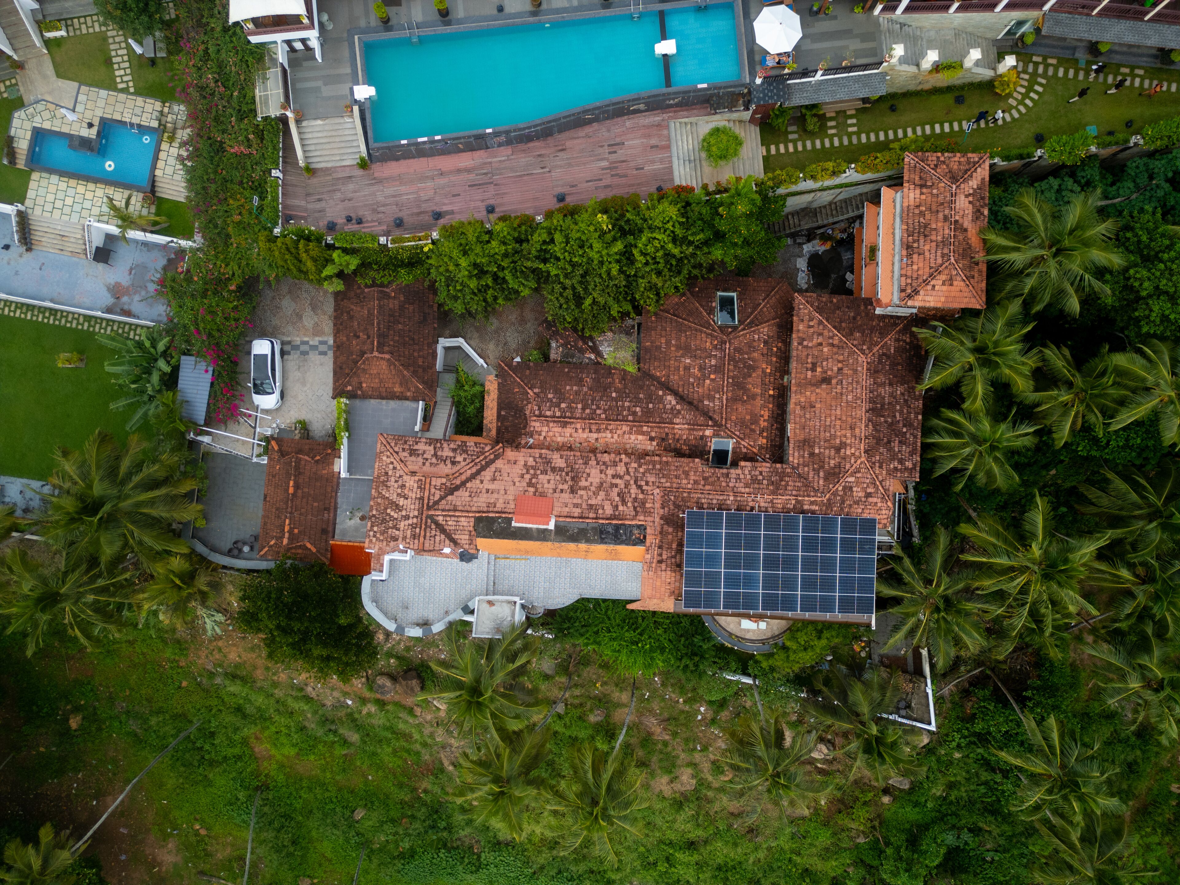 An aerial view of a residential area with a swimming pool, solar panels, and lush greenery.