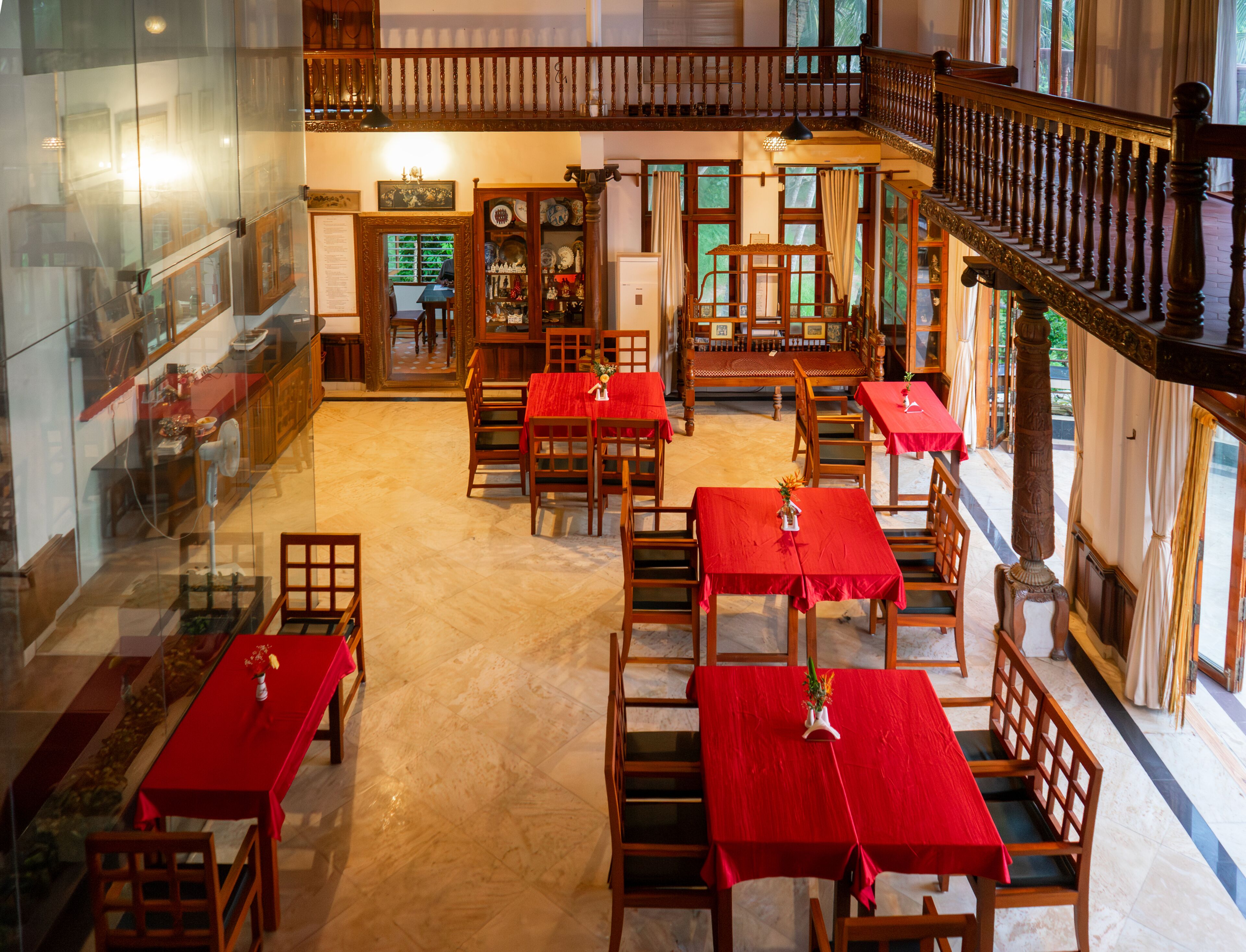 A spacious dining area with multiple tables and chairs, a balcony with a wooden railing, and a view of the outside through large windows.