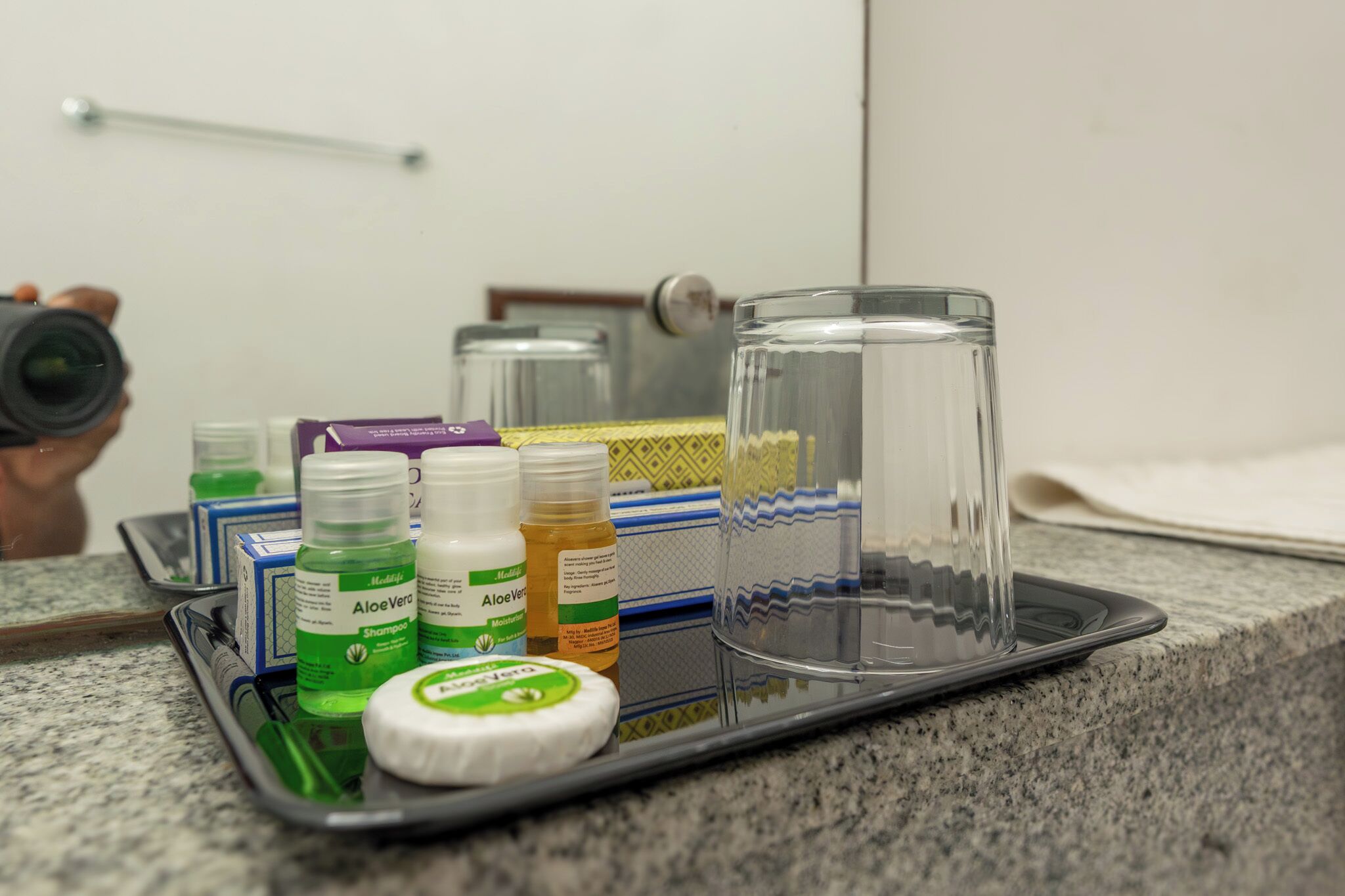 Una encimera de baño con una bandeja que contiene artículos de tocador, un vaso y un espejo que refleja un perchero.