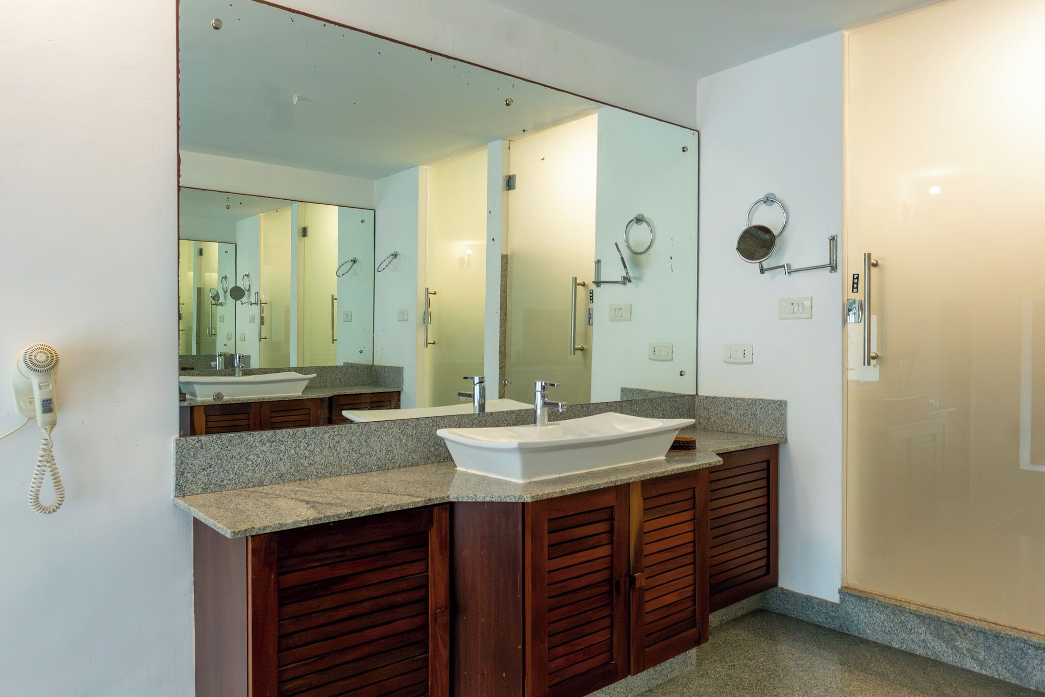 A bathroom with a large mirror, a white sink, wooden cabinets, and a shower area.