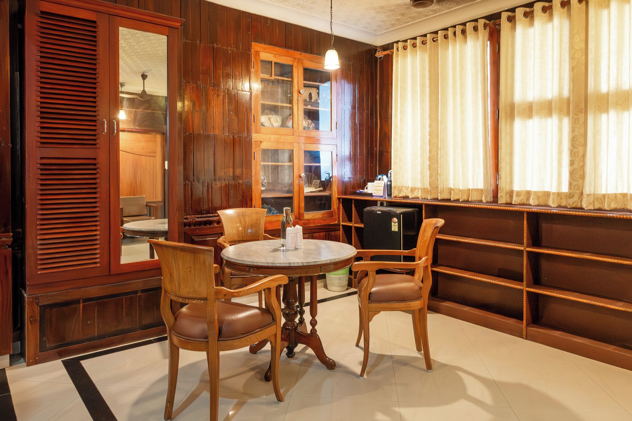 A dining area with a round table, two chairs, a cabinet with glass doors, and a shelf with items.