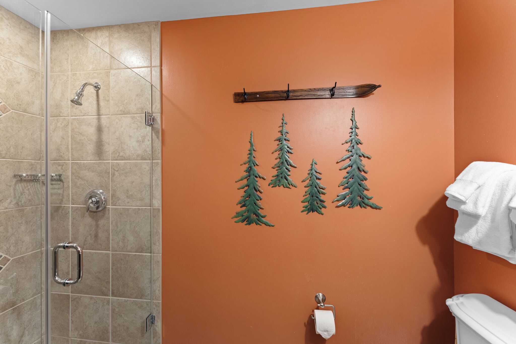 Un baño con cabina de ducha de vidrio, un perchero con asa de madera y tres adhesivos de hojas verdes en la pared.