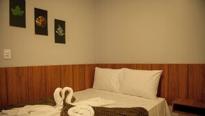 A hotel room with a wooden headboard, a bed with white linens, and two towels arranged in a heart shape on the bed. - Apto c Churrasqueira e Piscina a 100m da Praia (Japaratinga)