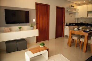 Un appartement moderne doté d’un téléviseur à écran plat, de portes en bois, d’un coin repas avec une table et des chaises, ainsi que d’une petite table blanche agrémentée d’une plante.