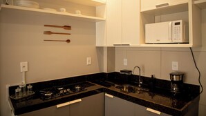 A modern kitchen with a gas stove, black granite countertop, white cabinets, a microwave, and a sink. - Apto c Churrasqueira e Piscina a 100m da Praia (Japaratinga)