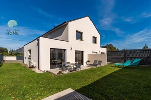 Et moderne hus i to etager med en stor terrasse, en lukket baghave og en klar blå himmel.