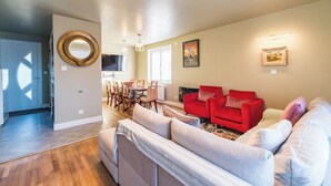 Un salon avec un canapé, des fauteuils rouges, un coin repas comprenant des chaises et une table, et un téléviseur fixé au mur.