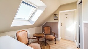 Une pièce chaleureuse avec un plafond en pente, une lucarne, une table ronde en bois, deux fauteuils rembourrés et une porte blanche.