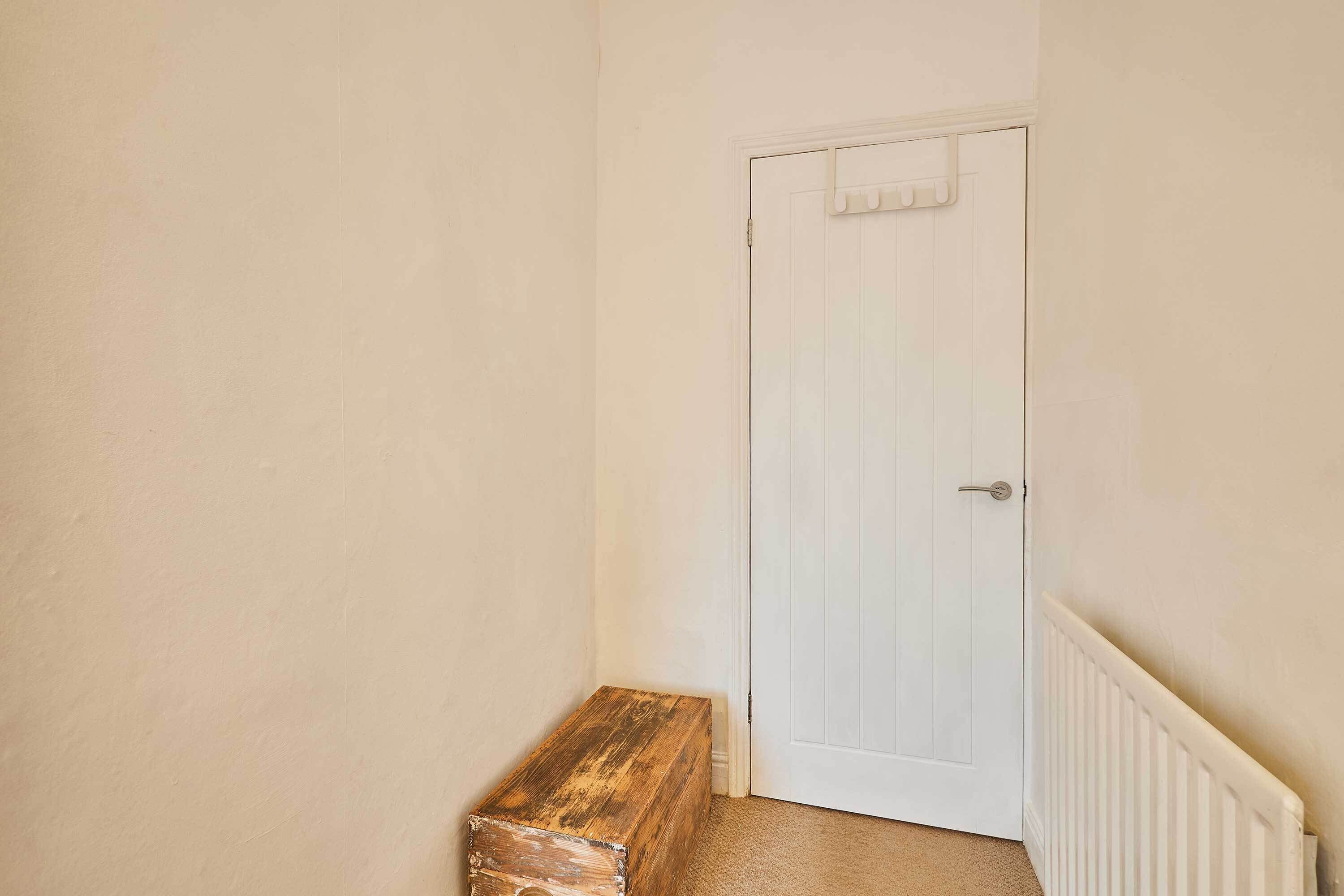 A narrow hallway with a white door and a wooden bench.