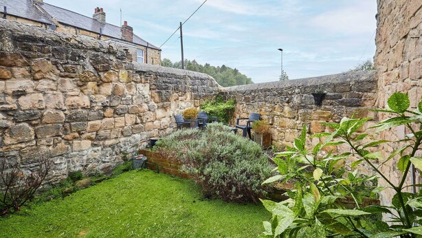 A stone-walled courtyard with a grassy area and a small seating arrangement. - Host Stay The Reading Room (Hexham)