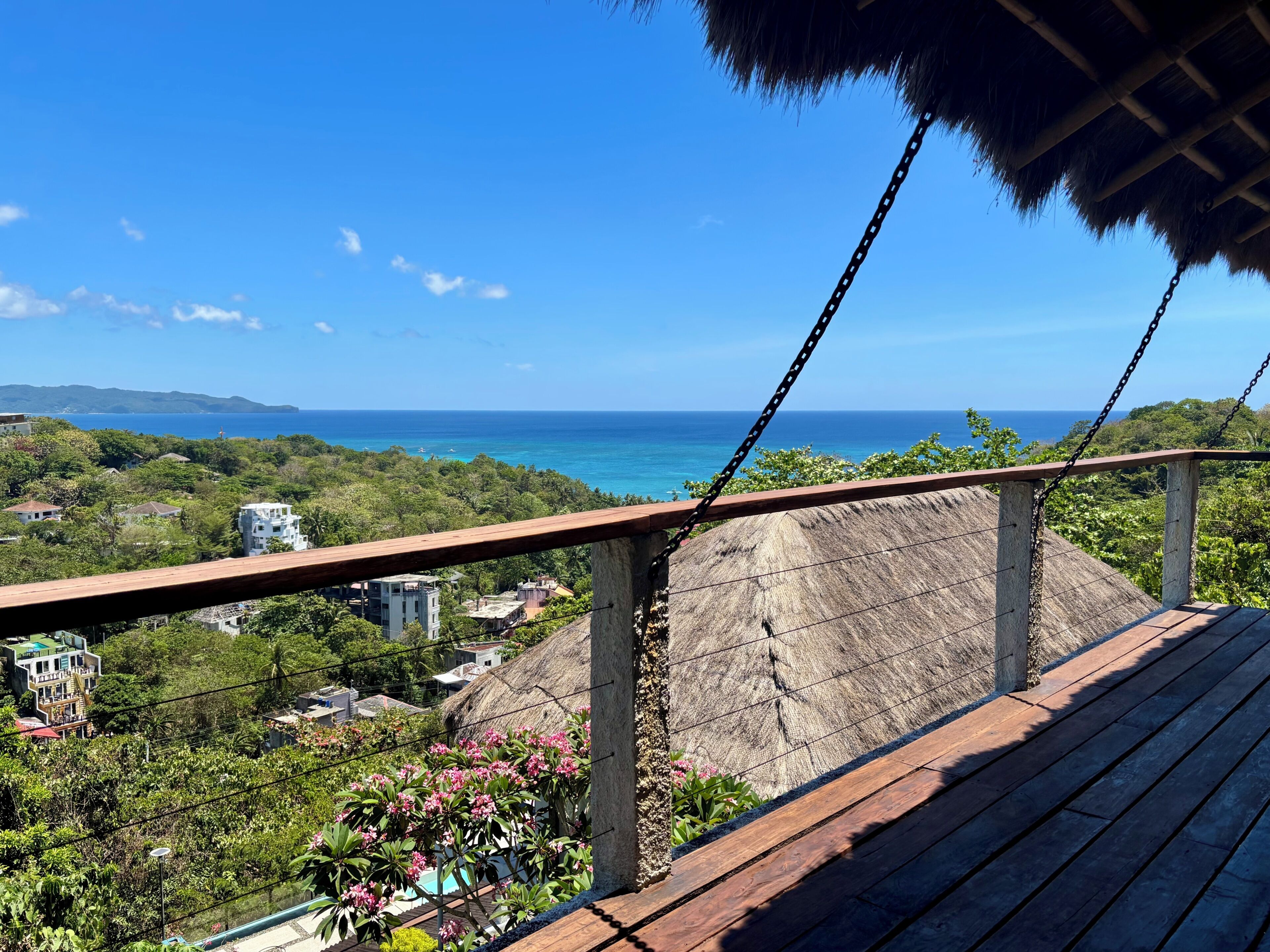 Une terrasse en bois offrant une vue sur l’océan, surmontée d’une structure à toit de chaume.