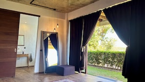 A bedroom with a bed, a small table, a mirror, and a view of a garden. - Villa JuPITER, Boracay, ocean view holiday home with pool (Malay)