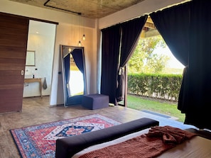 A bedroom with a bed, a small table, a mirror, and a view of a garden.