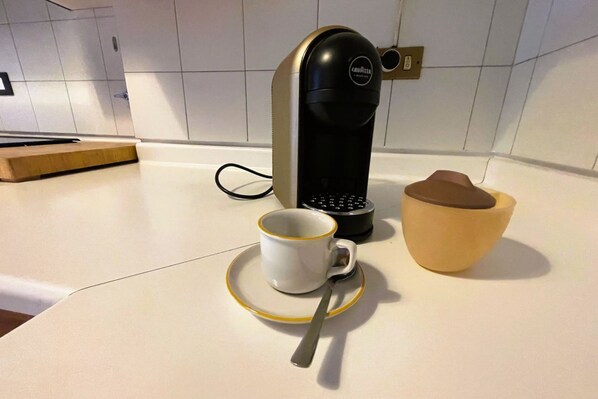 Une machine à café, une tasse blanche avec une cuillère et un bol en bois, le tout posé sur un plan de travail de cuisine.