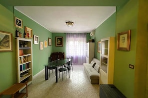 A dining area with a table and chairs, a sofa, a bookshelf, and framed pictures on the walls.
