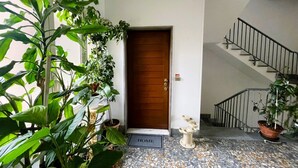 Ein Hauseingang mit Holztür, Fußmatte, einer Treppe mit Metallgeländer und Topfpflanzen.