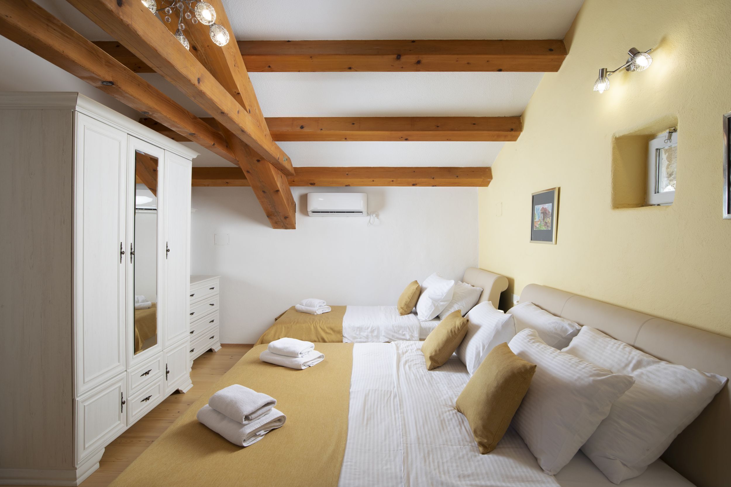 Ein Schlafzimmer mit zwei Betten, Holzbalken, einem weißen Kleiderschrank und einer Deckenleuchte.